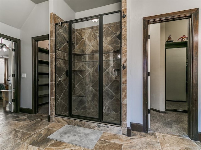 full bath featuring stone tile floors, a stall shower, lofted ceiling, and baseboards