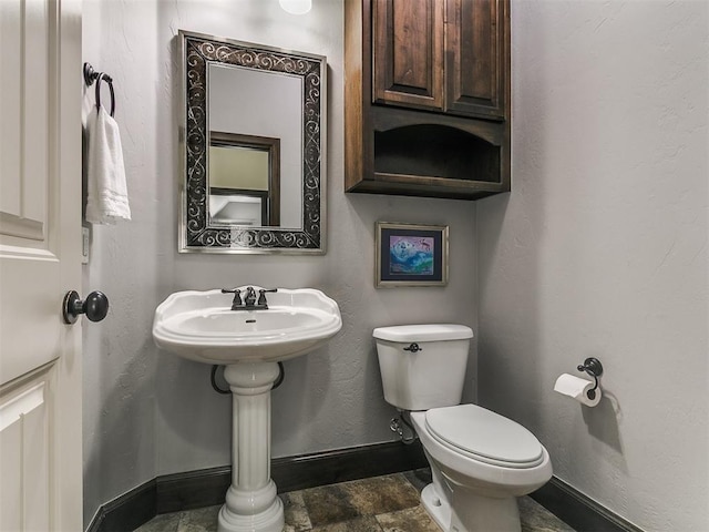 half bath with stone finish floor, toilet, a textured wall, and baseboards