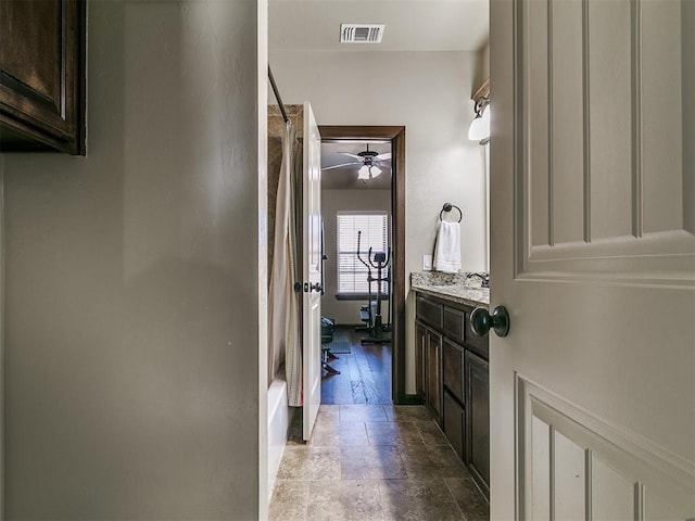 bathroom with visible vents, a ceiling fan, stone tile floors, shower / tub combo, and vanity