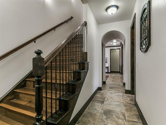 stairway with arched walkways, stone finish floor, and baseboards