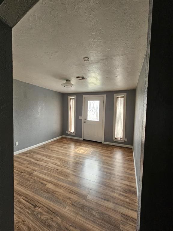 foyer with visible vents, baseboards, dark wood-style floors, and a textured wall