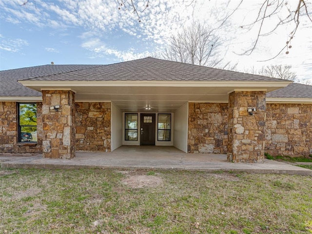 view of exterior entry with a carport, stone siding, and roof with shingles