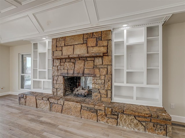 unfurnished living room featuring built in shelves, coffered ceiling, wood finished floors, a stone fireplace, and baseboards