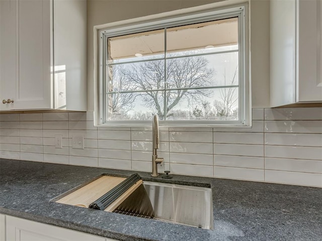 details with tasteful backsplash, white cabinetry, and a sink