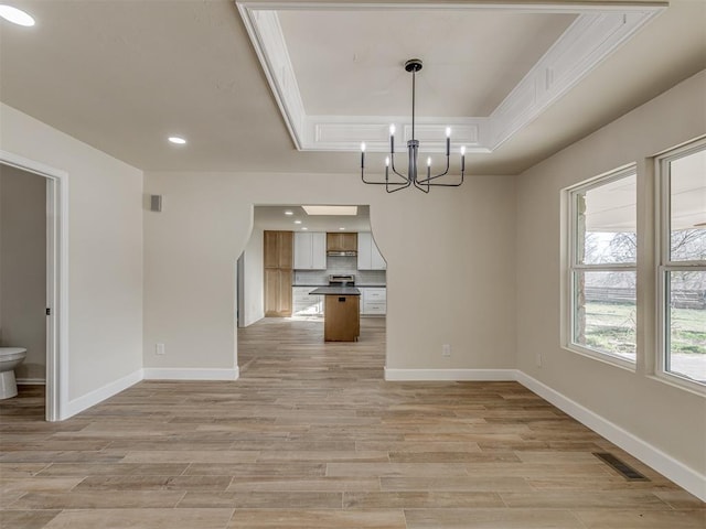 unfurnished dining area featuring visible vents, a tray ceiling, light wood-style floors, an inviting chandelier, and baseboards