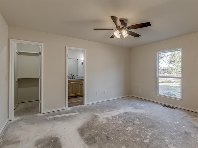 unfurnished bedroom with visible vents, a walk in closet, a ceiling fan, ensuite bath, and baseboards