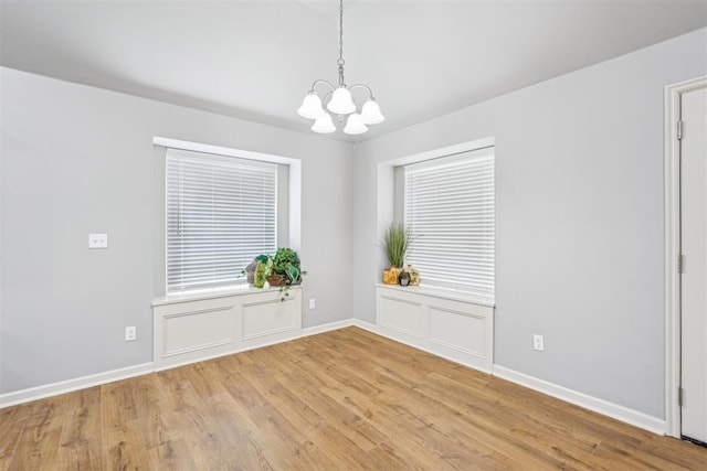 spare room with light wood-style floors, baseboards, and a chandelier