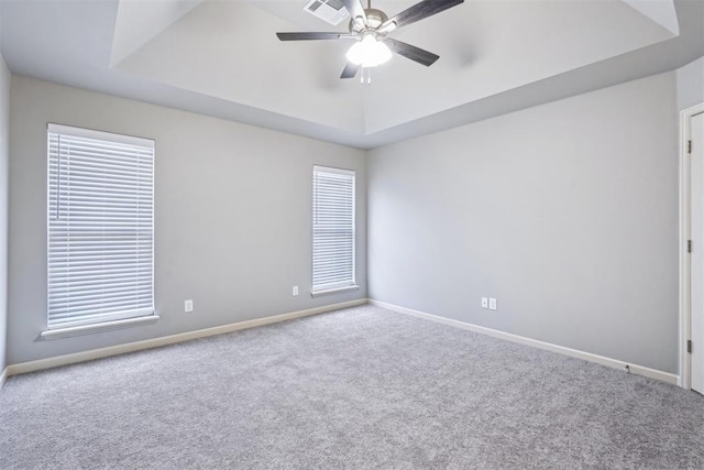 carpeted empty room with visible vents, a raised ceiling, and baseboards