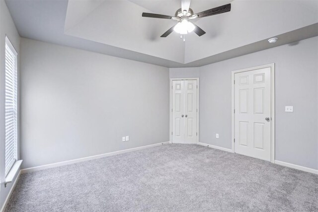 unfurnished bedroom featuring a raised ceiling, a closet, carpet floors, baseboards, and ceiling fan