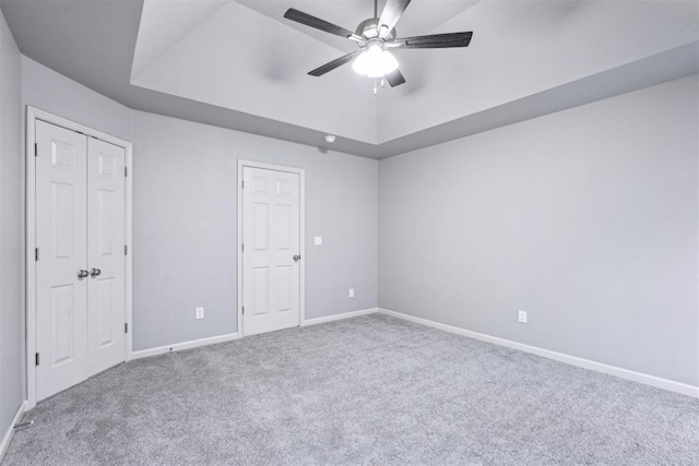 unfurnished bedroom featuring ceiling fan, baseboards, carpet, and a tray ceiling