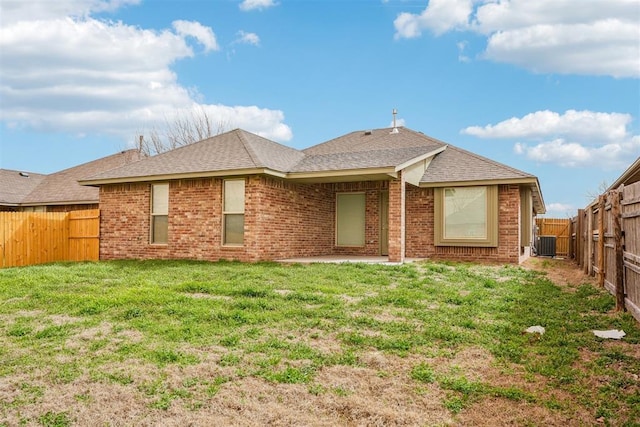 rear view of house featuring a fenced backyard, cooling unit, a yard, roof with shingles, and brick siding