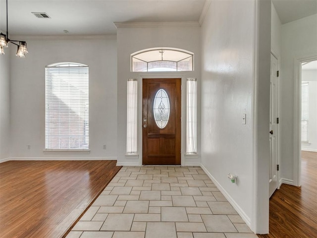 foyer entrance with visible vents, a notable chandelier, light wood-style flooring, and crown molding