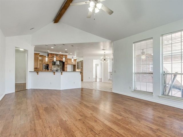 unfurnished living room with light wood-type flooring, beam ceiling, high vaulted ceiling, ceiling fan with notable chandelier, and baseboards