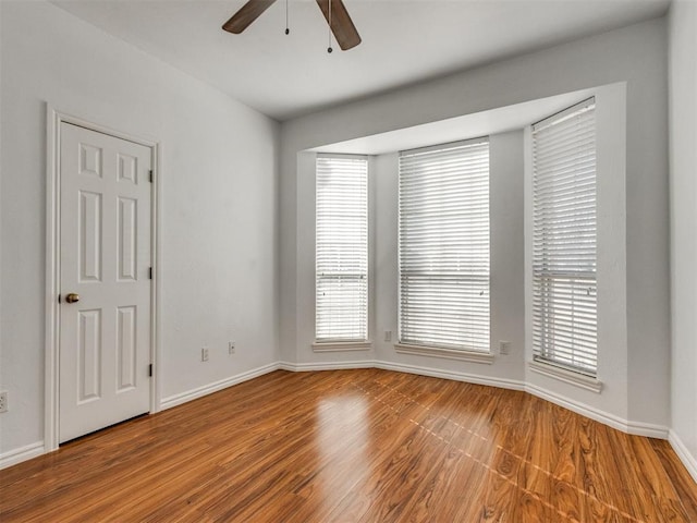 empty room featuring a healthy amount of sunlight, baseboards, ceiling fan, and wood finished floors