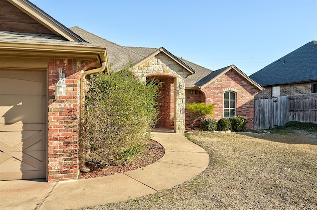 view of front of home featuring fence, brick siding, and roof with shingles