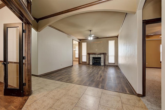 unfurnished living room with tile patterned flooring, crown molding, a fireplace, arched walkways, and a ceiling fan