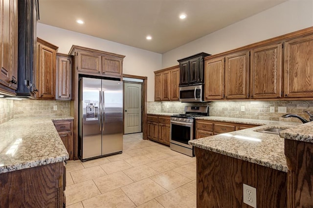 kitchen featuring light tile patterned floors, light stone countertops, a sink, appliances with stainless steel finishes, and backsplash