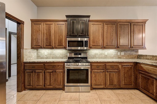 kitchen featuring light tile patterned floors, backsplash, stainless steel appliances, and light stone counters