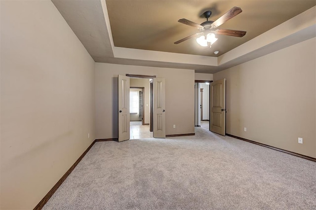 unfurnished bedroom with baseboards, a raised ceiling, light colored carpet, and ceiling fan