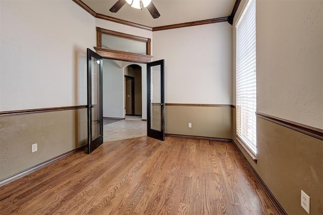 empty room featuring arched walkways, crown molding, a ceiling fan, and wood finished floors