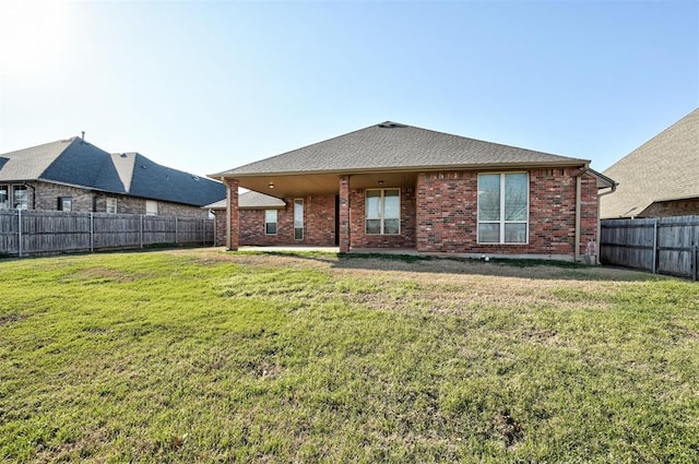 back of house featuring a yard, brick siding, a fenced backyard, and a shingled roof