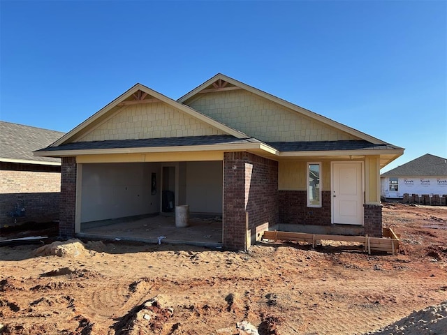 view of front of home featuring a garage, brick siding, roof with shingles, and a patio area