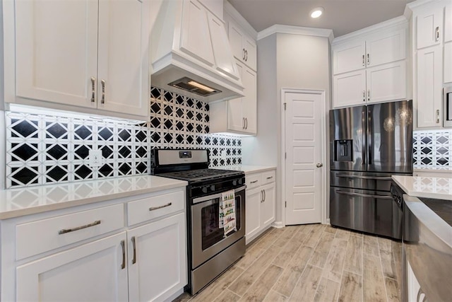 kitchen with white cabinets, light countertops, appliances with stainless steel finishes, premium range hood, and tasteful backsplash