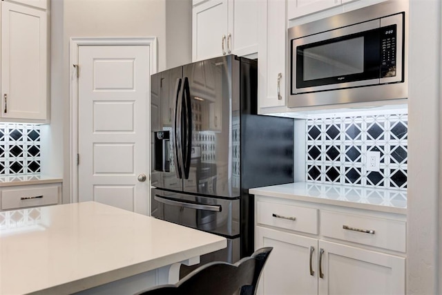 kitchen with light countertops, black refrigerator with ice dispenser, white cabinets, and stainless steel microwave