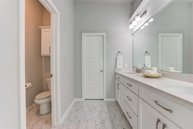 bathroom featuring a sink, double vanity, toilet, and baseboards