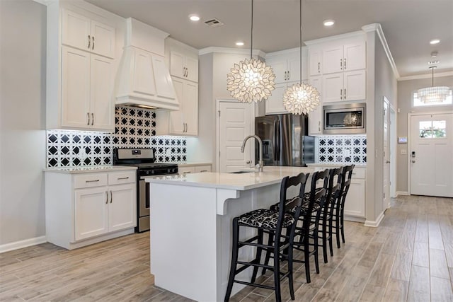 kitchen with premium range hood, white cabinetry, stainless steel appliances, and a sink