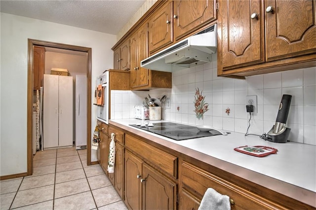 kitchen featuring under cabinet range hood, a textured ceiling, brown cabinetry, light tile patterned floors, and black electric cooktop