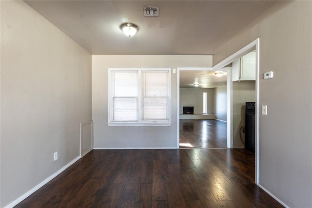 unfurnished room featuring visible vents, a fireplace with raised hearth, baseboards, and wood finished floors