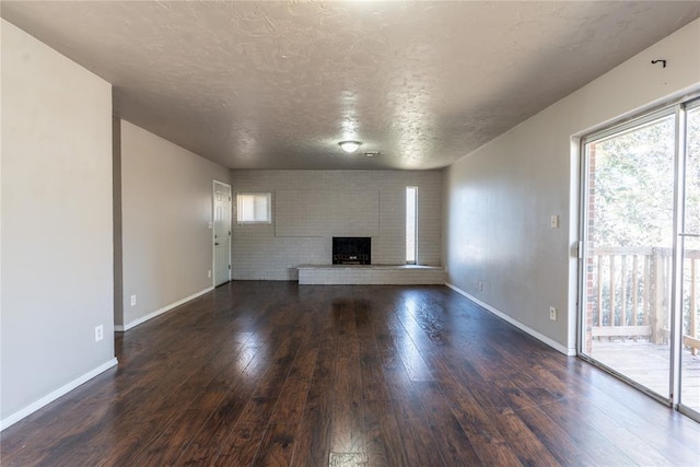 unfurnished living room featuring dark wood-type flooring, a brick fireplace, baseboards, and a textured ceiling