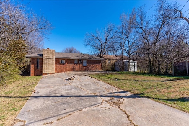 view of front of home with driveway, a front yard, crawl space, brick siding, and a chimney