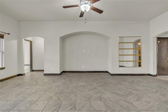 unfurnished room with a ceiling fan, arched walkways, and baseboards