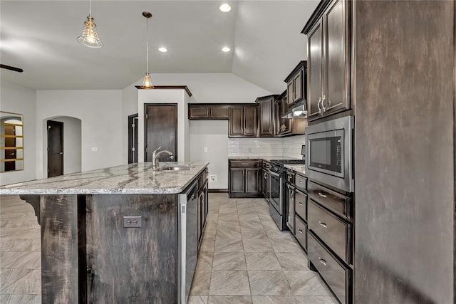 kitchen with light stone countertops, stainless steel appliances, dark brown cabinets, under cabinet range hood, and tasteful backsplash