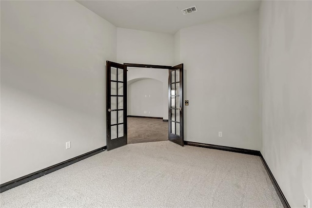 carpeted spare room with french doors, baseboards, arched walkways, and visible vents