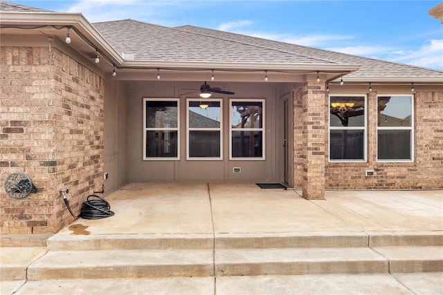 entrance to property featuring a patio area, brick siding, roof with shingles, and ceiling fan