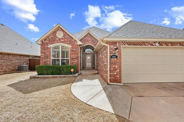 view of front of property featuring cooling unit, roof with shingles, concrete driveway, a garage, and brick siding