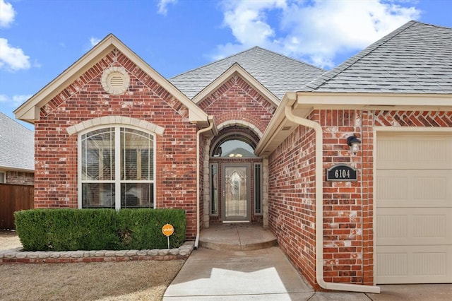 view of exterior entry featuring brick siding, a shingled roof, and a garage