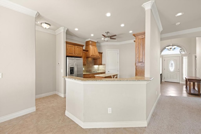 kitchen featuring tasteful backsplash, light stone countertops, ornamental molding, ceiling fan with notable chandelier, and stainless steel fridge