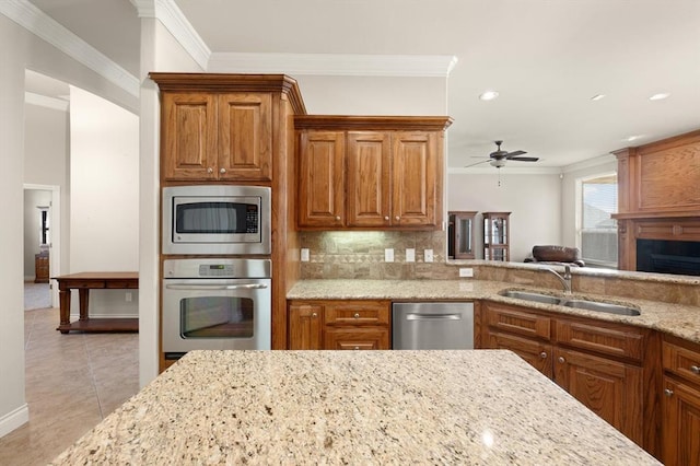 kitchen featuring ornamental molding, light stone counters, decorative backsplash, appliances with stainless steel finishes, and a sink