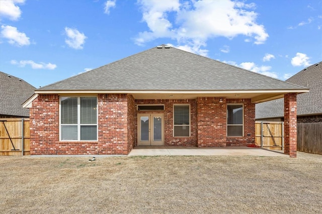 back of house featuring brick siding, fence, roof with shingles, french doors, and a patio area