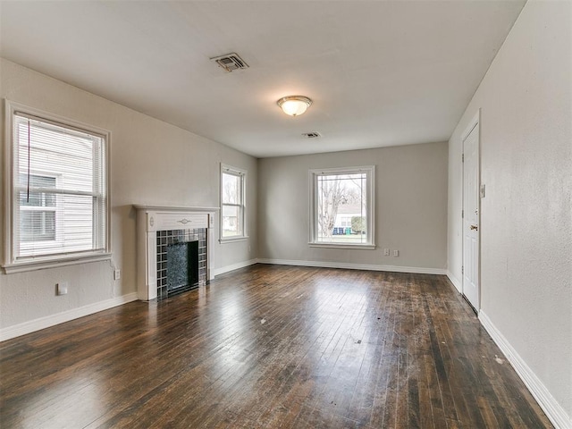 unfurnished living room featuring a tiled fireplace, hardwood / wood-style flooring, baseboards, and visible vents