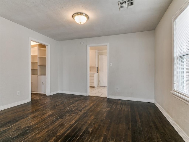 empty room with visible vents, baseboards, a textured ceiling, and hardwood / wood-style flooring