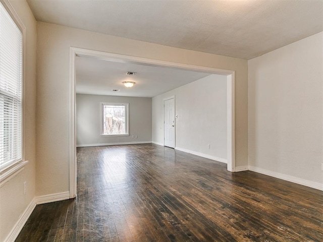 spare room featuring visible vents, baseboards, and dark wood-style floors