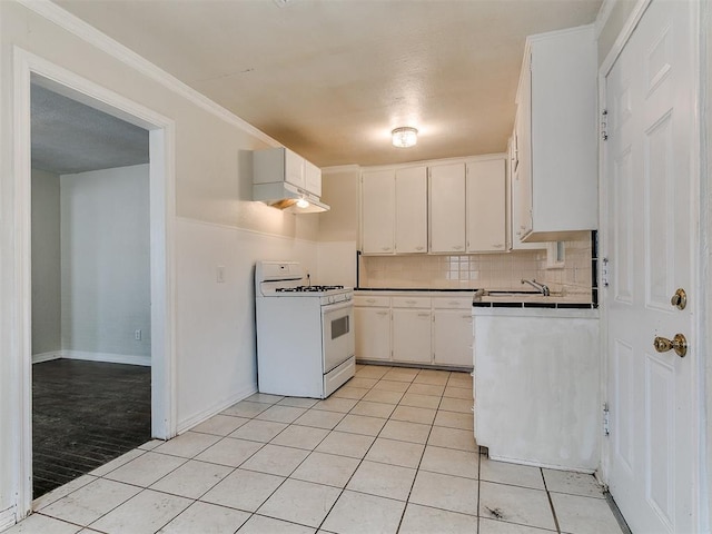 kitchen featuring backsplash, white range with gas stovetop, ornamental molding, light tile patterned floors, and white cabinetry