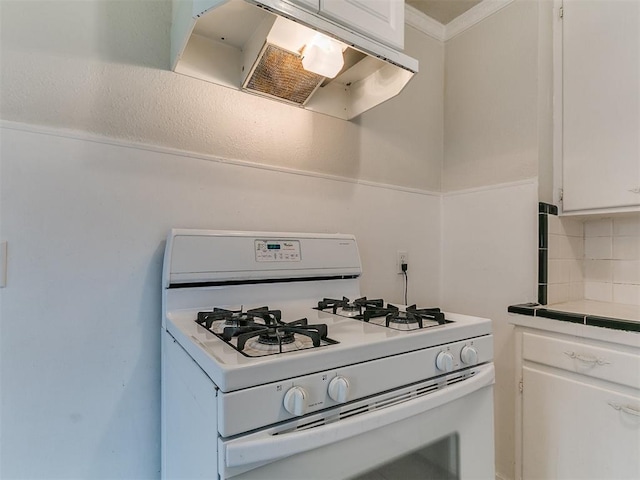 kitchen featuring tasteful backsplash, under cabinet range hood, tile countertops, white gas range, and white cabinetry