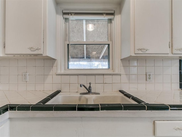 kitchen with white cabinetry, tile countertops, backsplash, and a sink