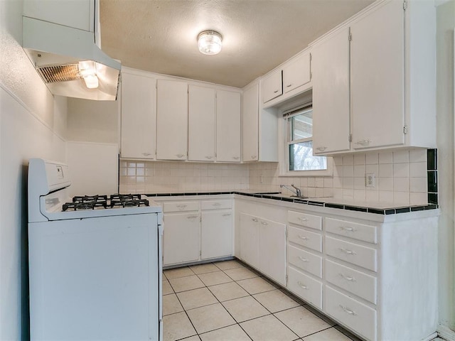 kitchen featuring under cabinet range hood, tasteful backsplash, white range with gas stovetop, and tile counters